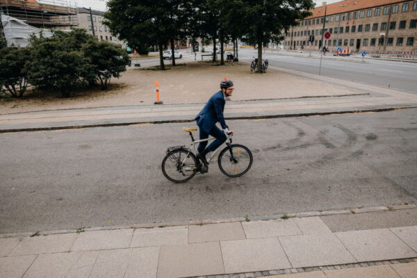 A high-angle view of a man wearing a blue business suit and a cycling helmet riding his bicycle down a city street paved with asphalt.