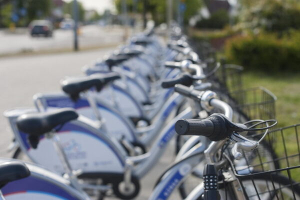 A row of parked public sharing bicycles with a shallow depth of field focusing on the front handlebar.