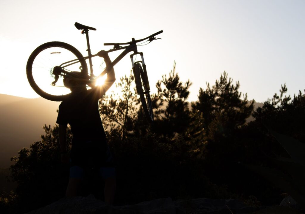 Silhouette of a person holding a bicycle above their shoulder at sunset.