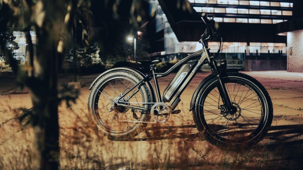 A black electric fat-tire bike parked outdoors in front of a lit building.