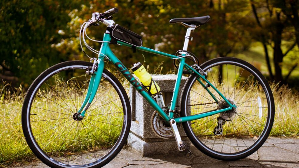 A teal Giant brand hybrid bicycle parked outdoors with a yellow water bottle attached.