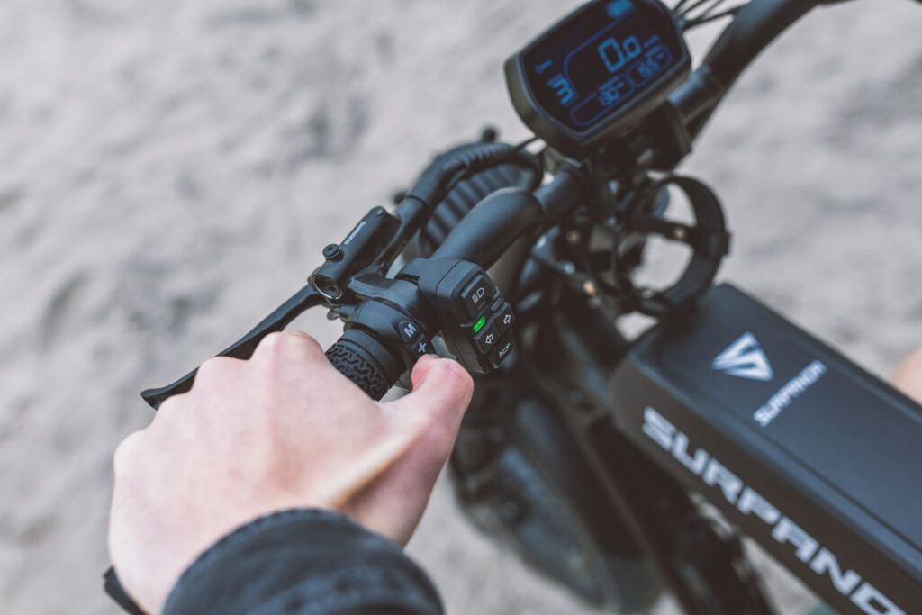 First-person view of a hand pressing a button on the handlebar controls of a Surpanrx electric bike.